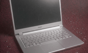 A professional technician using a microscope to identify and remove corrosion from an Acer Nitro motherboard after a liquid spill, shown on a solid light pink background for Atlantis repair services.