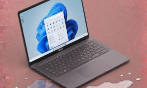 An Asus laptop motherboard undergoing professional ultrasonic cleaning and corrosion treatment for liquid damage, displayed on a solid light pink background for Atlantis UK-wide repair services.