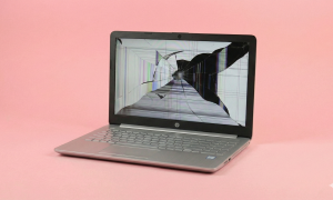 Professional studio photograph of a silver HP laptop with a severely smashed LED screen showing colourful vertical lines and black ink spots, isolated on a light pink background for Atlantis Canterbury repair services.