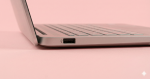 Professional studio photograph close-up of the side profile of a silver laptop, showing a USB port, set against a solid light pink background for Atlantis USB port repair services