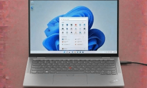 A professional technician replacing a Lenovo ThinkPad DC power jack on a motherboard, displayed on a solid light pink background for Atlantis UK-wide repair services.