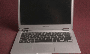 A close-up of a precision-engineered steel hinge being reinforced and mounted into a Lenovo laptop chassis, shown on a solid light pink background for Atlantis repair services.
