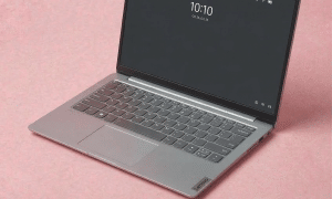 A professional Lenovo ThinkPad being serviced at the Atlantis workshop in Canterbury, displayed on a solid light pink background for UK-wide mail-in repair services.