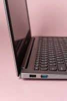 Professional 1:1 square studio photograph of a silver Lenovo laptop featuring a heavily cracked and shattered screen, set against a solid light pink background for Atlantis laptop screen repair services.