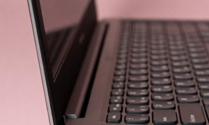 Professional 1:1 square studio photograph of a silver Lenovo laptop featuring a heavily cracked and shattered screen, set against a solid light pink background for Atlantis laptop screen repair services.