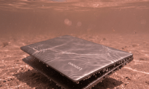 A professional technician using a digital microscope and precision tools to treat corrosion on a Lenovo motherboard after a liquid spill, shown on a solid light pink background for Atlantis repair services.