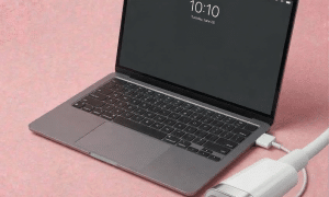 A professional technician replacing a MacBook Air MagSafe 3 charging port and secondary USB-C I/O board, displayed on a solid light pink background for Atlantis UK-wide repair services.