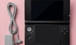 A premium replacement DC power jack and charging port for a Nintendo 3DS XL, shown on a solid light pink background for Atlantis UK-wide console repair services.