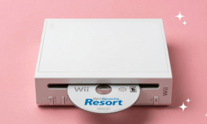 A premium replacement optical disc drive laser and motor assembly for a Nintendo Wii, displayed on a solid light pink background for Atlantis UK-wide console repair services.