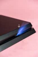 Professional 1:1 square studio photograph of the rear profile of a black PlayStation 4 console, highlighting the metal HDMI port against a solid light pink background for Atlantis console repair services.