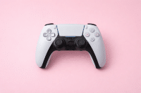 Professional 1:1 square studio photograph of a black PlayStation 4 DualShock controller and a white PlayStation 5 DualSense controller, set against a solid light pink background for Atlantis controller repair services.