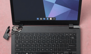 A replacement heavy-duty steel hinge and reinforced plastic lid mounting bracket for a Toshiba Satellite, displayed on a solid light pink background for Atlantis UK-wide repair services.