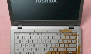 A Toshiba laptop motherboard undergoing professional ultrasonic cleaning and corrosion removal, displayed on a solid light pink background for Atlantis UK-wide repair services.