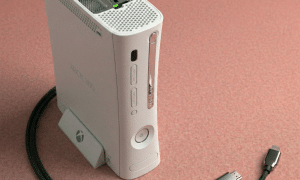 Close-up of a replacement HDMI socket and the rear video output interface of an Xbox 360 console, positioned on a solid light pink background for Atlantis repair services.