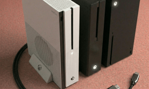 Close-up of the front power button and LED indicator of an Xbox One S and X console, positioned on a solid light pink background for Atlantis repair services.