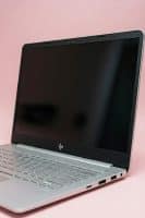 Close-up macro photograph of a physically damaged HDMI and USB 3.0 port on a silver HP laptop, featuring bent internal pins and a cracked chassis, set against a light pink studio background.
