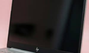 Close-up macro photograph of a physically damaged HDMI and USB 3.0 port on a silver HP laptop, featuring bent internal pins and a cracked chassis, set against a light pink studio background.