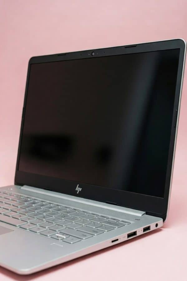 Close-up macro photograph of a physically damaged HDMI and USB 3.0 port on a silver HP laptop, featuring bent internal pins and a cracked chassis, set against a light pink studio background.