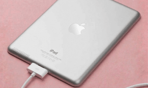 A professional technician replacing the dual-lens camera module and LiDAR scanner on an iPad Pro, displayed on a solid light pink background for Atlantis UK-wide repair services.