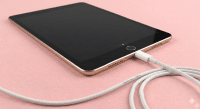A premium replacement Lightning charging port and dock connector flex cable for an iPad, shown on a solid light pink background for Atlantis repair services.