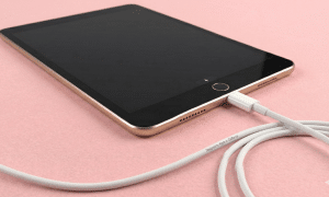 A premium replacement Lightning charging port and dock connector flex cable for an iPad 6th, 7th, 8th, or 9th generation, shown on a solid light pink background for Atlantis repair services.