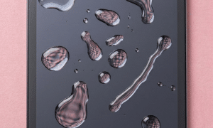 An iPad Mini motherboard undergoing professional ultrasonic cleaning and micro-soldering to fix liquid damage, displayed on a solid light pink background for Atlantis repair services.