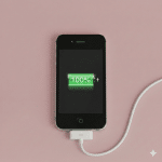 Close-up of the 30-pin charging port and dock connector on an Apple iPhone 4 and 4S, set against a solid light pink background for Atlantis repair services.