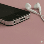 Close-up of the 3.5mm headphone jack on the top edge of an Apple iPhone 4, positioned on a solid light pink background for Atlantis repair services.