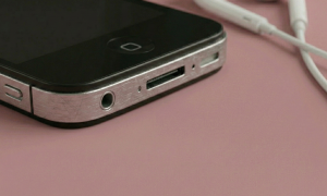 Close-up of the 3.5mm headphone jack on the top edge of an Apple iPhone 4, positioned on a solid light pink background for Atlantis repair services.