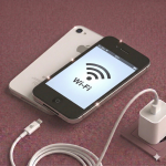 Close-up of the internal Wi-Fi and Bluetooth integrated circuit chip on an iPhone 4S logic board being professionally reflowed, positioned on a solid light pink background for Atlantis repair services.