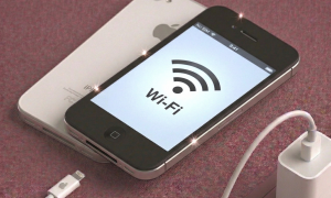 Close-up of the internal Wi-Fi and Bluetooth integrated circuit chip on an iPhone 4S logic board being professionally reflowed, positioned on a solid light pink background for Atlantis repair services.