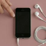 Close-up of the 3.5mm headphone jack socket on the bottom of an Apple iPhone 5, positioned on a solid light pink background for Atlantis repair services.