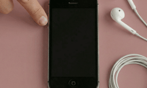 Close-up of the 3.5mm headphone jack socket on the bottom of an Apple iPhone 5, positioned on a solid light pink background for Atlantis repair services.