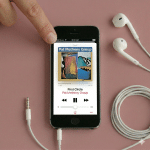 Close-up of the speaker grilles on the bottom edge of an Apple iPhone 5, positioned on a solid light pink background for Atlantis repair services.