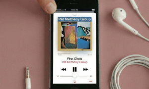 Close-up of the speaker grilles on the bottom edge of an Apple iPhone 5, positioned on a solid light pink background for Atlantis repair services.
