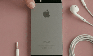 Close-up of the power button on the top edge of an Apple iPhone 5, positioned on a solid light pink background for Atlantis repair services.
