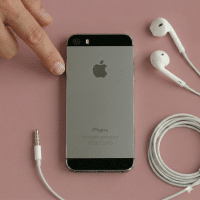 Close-up of the rear camera lens and LED flash of an Apple iPhone 5, positioned on a solid light pink background for Atlantis repair services.