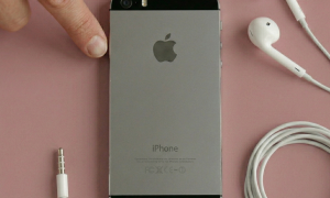 Close-up of the rear camera lens and LED flash of an Apple iPhone 5, positioned on a solid light pink background for Atlantis repair services.