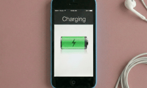 Close-up of the Lightning charging port and dock connector assembly for an iPhone 5, 5S, 5C, and 5SE, positioned on a solid light pink background for Atlantis repair services.