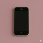 Close-up of an Apple iPhone 5S with a shattered and cracked glass screen, positioned on a solid light pink background for Atlantis repair services.