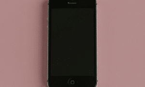 Close-up of an Apple iPhone 5S with a shattered and cracked glass screen, positioned on a solid light pink background for Atlantis repair services.