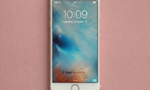 Close-up of the Lightning charging port and headphone jack assembly for an Apple iPhone 6 and 6S, positioned on a solid light pink background for Atlantis repair services.