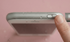 Close-up of the power and volume buttons on the side profile of an Apple iPhone 6 and 6S series handset, set against a solid light pink background for Atlantis repair services.