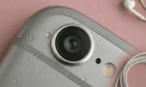 Close-up of the rear camera lens of an Apple iPhone 6S, showcasing the protective sapphire glass on a solid light pink background for Atlantis repair services.