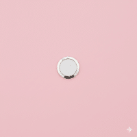 Professional 1:1 square studio photograph showing a close-up of the circular Home Button (Touch ID sensor) on the bottom bezel of a silver iPhone 7, set against a solid light pink background for Atlantis repair services.