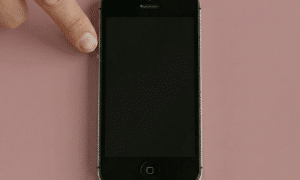 Close-up of the volume control buttons on the side of an iPhone, positioned on a solid light pink background for Atlantis repair services.