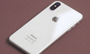 A high-quality replacement rear housing chassis with a glass back panel and integrated frame for the iPhone X, XR, and XS series, shown on a solid light pink background for Atlantis repair services.