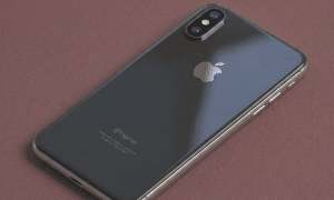 Close-up of a precision-cut sapphire glass replacement rear camera lens for the iPhone X, XR, and XS series, positioned on a solid light pink background for Atlantis repair services.