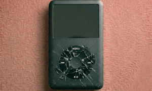 Close-up of a replacement white and black capacitive Click Wheel component for the Apple iPod Classic, positioned on a solid light pink background for Atlantis repair services.