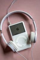 Professional 1:1 square studio photograph of the top profile of a silver Apple iPod Classic, focusing on the headphone jack socket against a solid light pink background for Atlantis repair services.